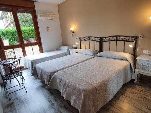 A cozy hotel room with twin beds, wooden floors, and a balcony view of greenery offers a serene retreat for travelers seeking relaxation.