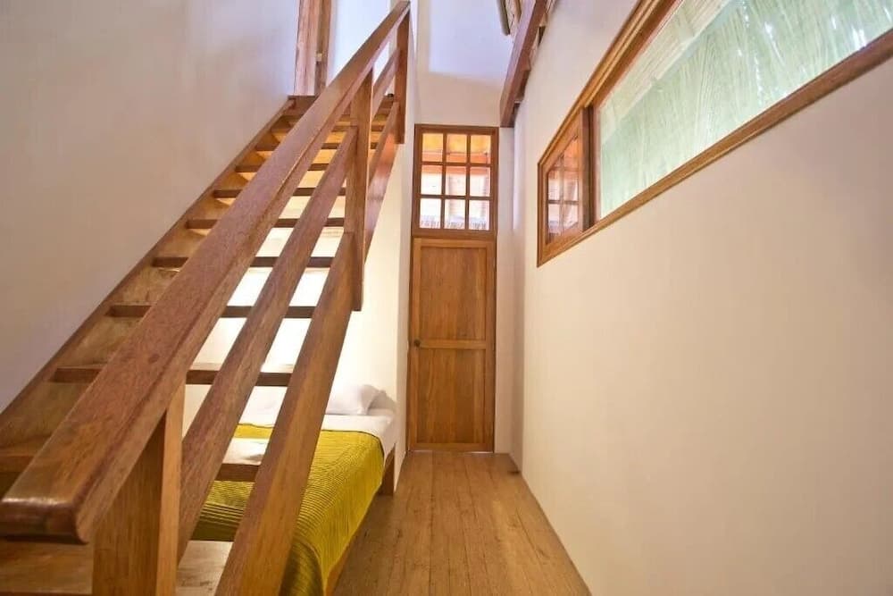 A cozy indoor scene featuring a wooden staircase leading to a loft bed, a rustic door with glass panels, and a serene atmosphere ideal for travelers seeking a quaint and intimate accommodation experience.