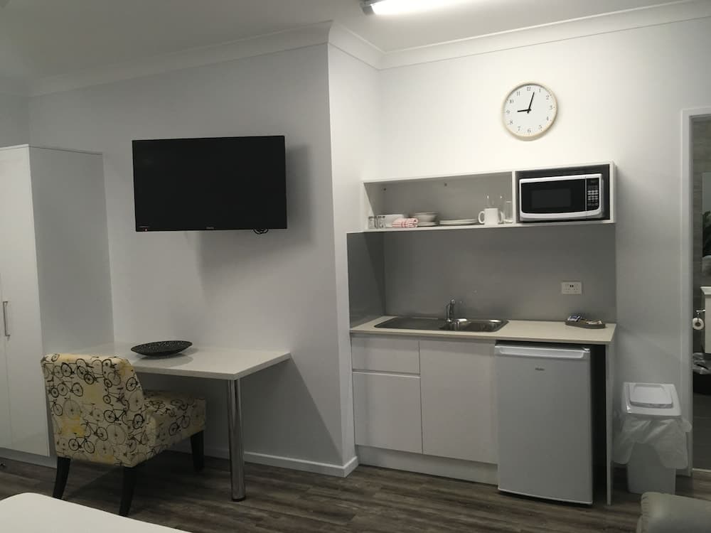 A cozy studio apartment features a compact kitchenette with a microwave and mini-fridge, a small dining area with a bicycle-patterned chair, and a wall-mounted TV, ideal for travelers seeking comfort and convenience in a minimalist setting.