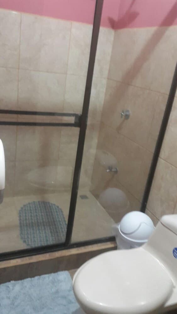 A cozy bathroom with pink walls, beige tiles, a glass shower enclosure, and a toilet featuring a blue sticker, ideal for travelers seeking compact and functional accommodations.