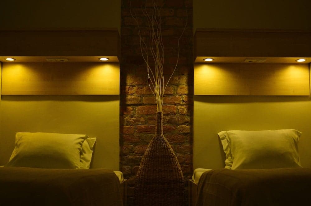A cozy hotel room features two neatly made beds under warm ambient lighting, separated by a rustic brick column adorned with a woven vase holding decorative branches, ideal for travelers seeking comfort and tranquility.