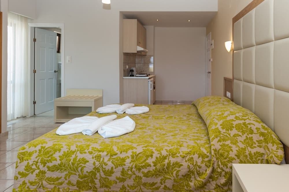 A cozy studio apartment features a neatly made bed with vibrant green bedding, a compact kitchenette, and soft lighting, ideal for travelers seeking comfort and convenience in a compact space.
