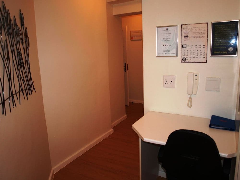 A cozy hotel room hallway features a small desk with a phone and chair, framed certificates on the wall, and a decorative metal art piece, ideal for travelers seeking a quiet workspace.