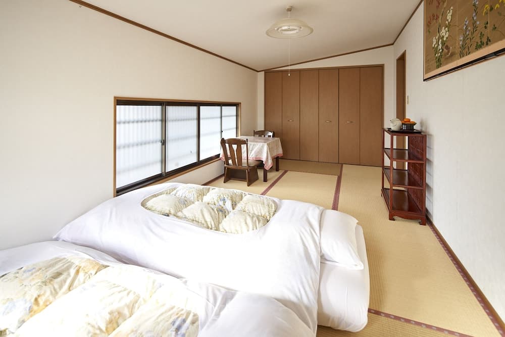 A serene Japanese-style guest room features tatami flooring, futon beds, wooden furniture, and shoji screens, ideal for travelers seeking a traditional and tranquil accommodation experience.