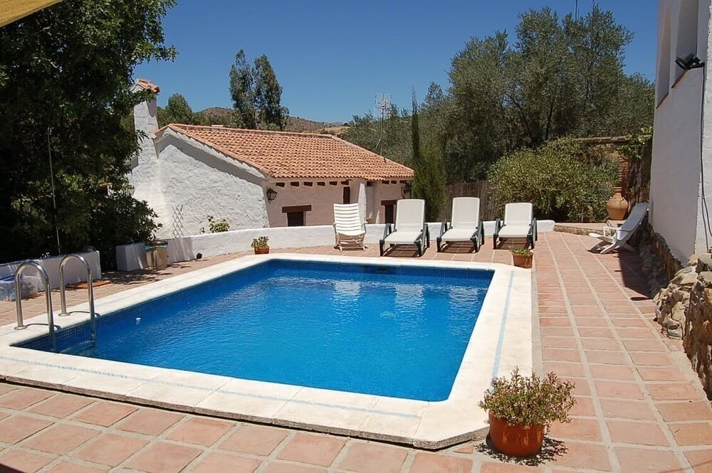 A serene private villa poolside scene features sun loungers on terracotta tiles, lush greenery, and a picturesque backdrop, ideal for relaxing retreats and family vacations.