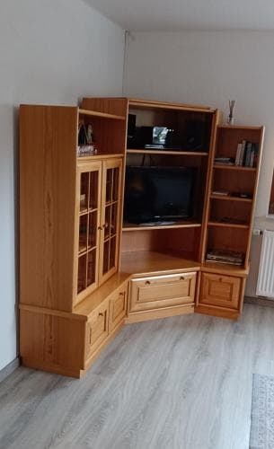 A cozy living room corner features a wooden entertainment unit housing books and a TV, set against light walls on a laminate floor, ideal for travelers seeking a comfortable and organized rental space.