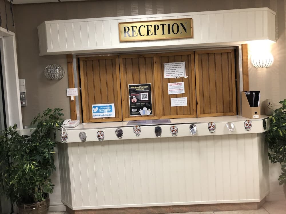 A cozy hotel reception adorned with sugar skull decorations and informative signs creates a welcoming atmosphere for travelers seeking assistance or local transport details.