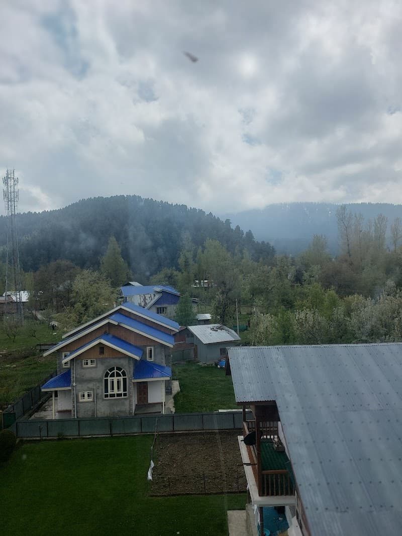 A serene view of a cozy cottage with blue roofs nestled amidst lush greenery under a cloudy sky, ideal for tranquil mountain retreats in Gulmarg.