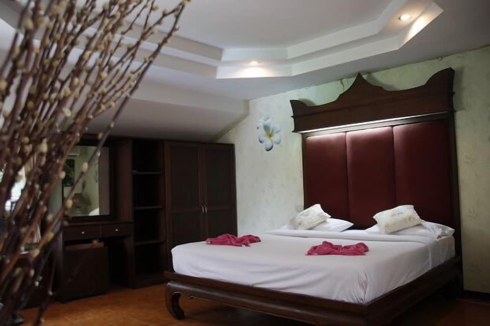 A cozy hotel bedroom features a neatly made bed with red accents, wooden furnishings, decorative branches, and soft lighting, ideal for travelers seeking comfort and relaxation.