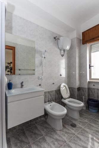 A modern bathroom with marble tiles, a bidet, toilet, sink, and large mirror offers a clean and functional space ideal for travelers seeking comfort in accommodations.