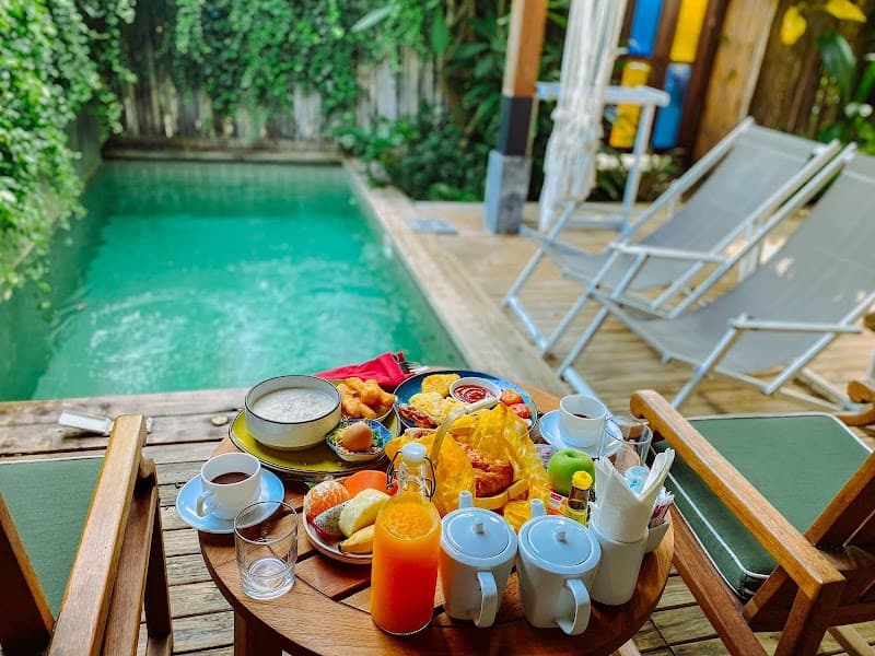 A serene tropical breakfast setup by a lush green poolside at a cozy resort in Thailand, featuring vibrant food and drinks on a wooden table, perfect for travelers seeking relaxation and luxury.