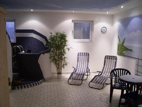 A cozy indoor relaxation area features a tiled floor, lounge chairs, a hot tub, and tropical plants, creating a serene atmosphere ideal for travelers seeking a tranquil spa experience.