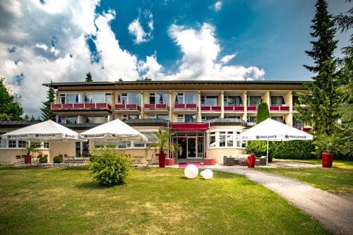 A serene resort hotel with a well-manicured lawn, outdoor seating under white canopies, and a backdrop of lush greenery and blue skies, ideal for a relaxing getaway or corporate retreat.