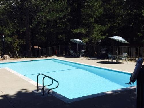 A serene outdoor swimming pool surrounded by lush trees offers a relaxing retreat with lounge chairs, umbrellas, and a shaded dining area, perfect for family vacations or weekend getaways.