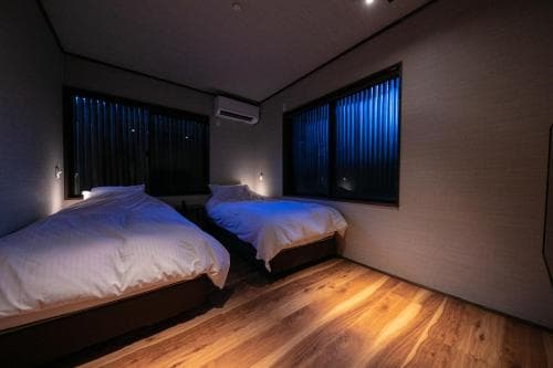 A cozy hotel room with two neatly made beds, wooden flooring, and blue-lit windows creates a serene atmosphere ideal for travelers seeking restful accommodations.