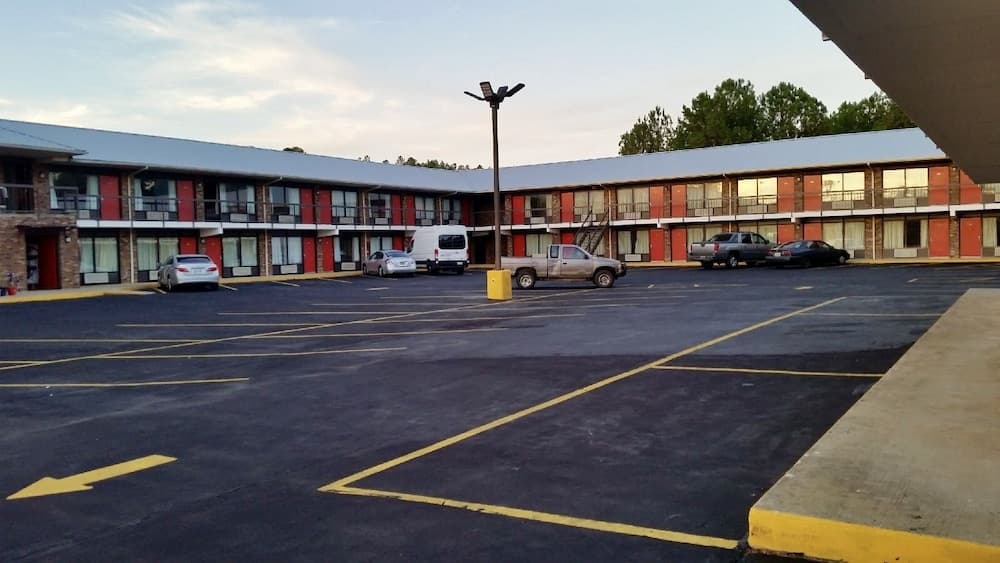A tranquil evening at a roadside motel features a spacious parking lot with parked cars, red-accented rooms, and a tall lamppost, ideal for travelers seeking budget-friendly accommodations.