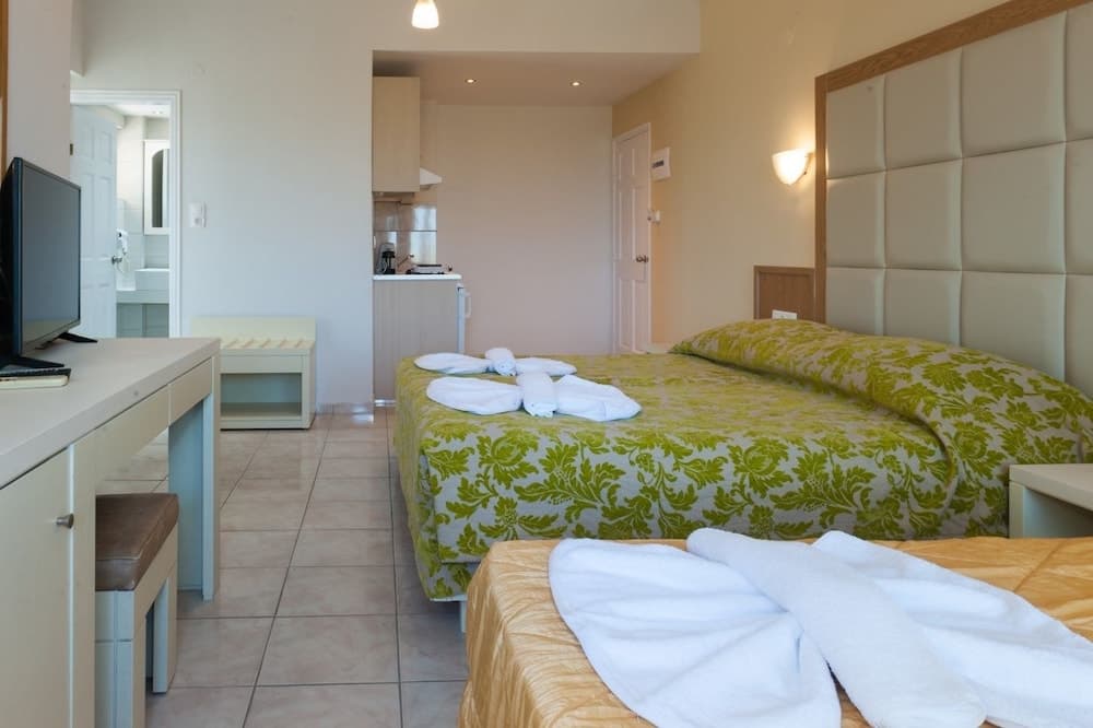A cozy hotel suite features a neatly made bed with green patterned bedding, a desk area, and an open bathroom, ideal for travelers seeking comfort and convenience.