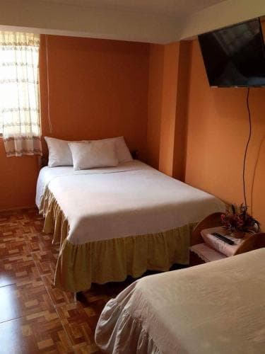 A cozy hotel room with warm orange walls, wooden flooring, neatly made beds, and a small TV, ideal for travelers seeking comfort and simplicity.