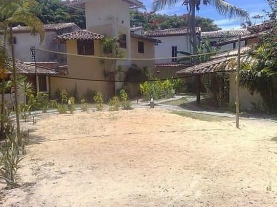 A serene tropical courtyard with sandy grounds, palm trees, and traditional tiled-roof buildings offers a peaceful retreat ideal for vacationers seeking relaxation.