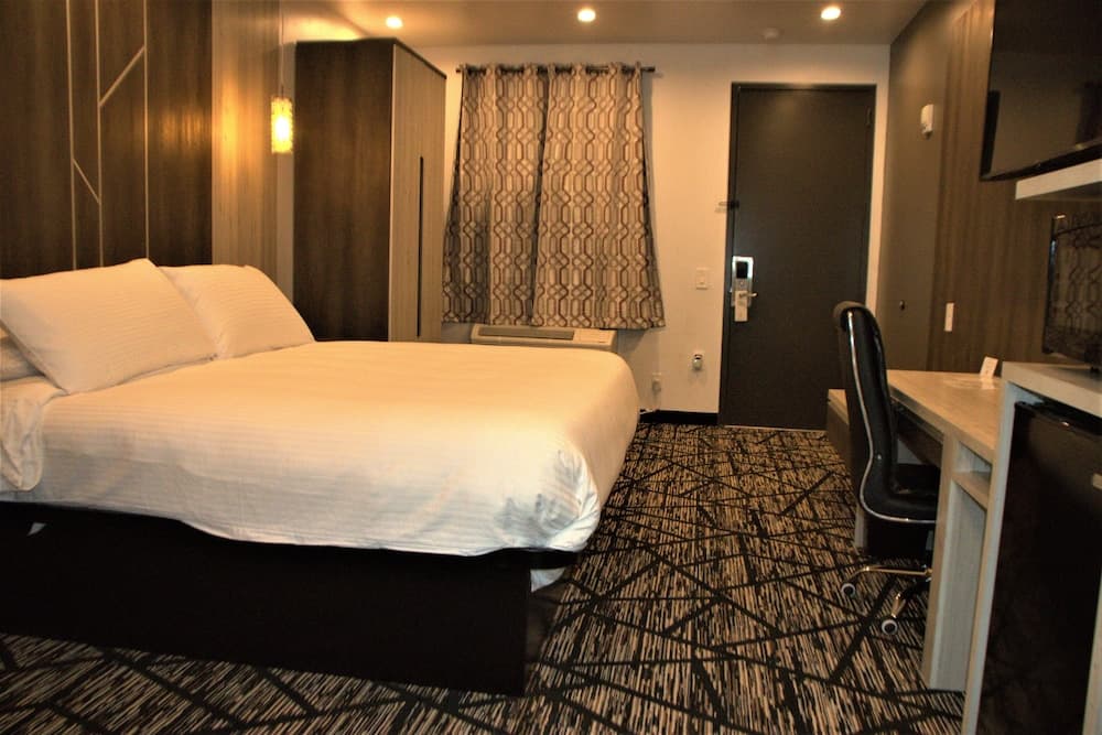 A cozy hotel room features a neatly made bed, patterned carpet, a desk with a chair, and soft lighting, ideal for travelers seeking comfort and functionality during their stay.
