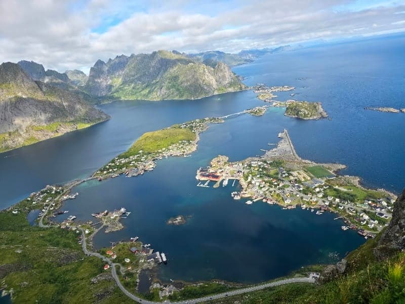 A breathtaking aerial view of a picturesque coastal village nestled among lush green hills and surrounded by deep blue waters, ideal for adventure seekers exploring the scenic Lofoten Islands in Norway.