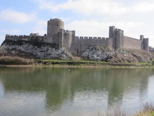 A serene medieval castle with robust stone walls and towers reflects in calm waters, offering a picturesque backdrop for history enthusiasts and photographers exploring ancient fortifications.