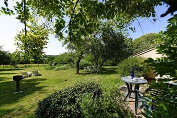 A serene outdoor garden scene with lush greenery, a small table set under a tree, and distant seating areas, ideal for a peaceful retreat or countryside vacation.