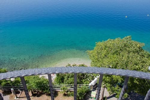 A serene coastal view from a balcony railing showcases turquoise waters, lush greenery, and a tranquil beach atmosphere, ideal for relaxing seaside getaways.