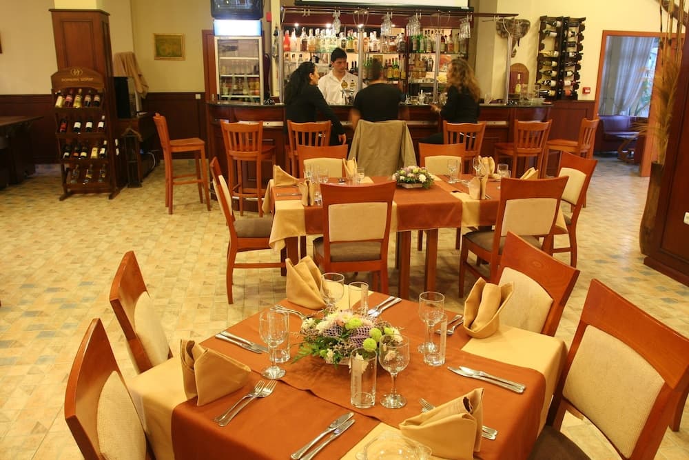 A cozy restaurant interior features warmly lit tables set with orange linens, floral centerpieces, and neatly arranged cutlery, creating an inviting atmosphere ideal for intimate dining experiences.