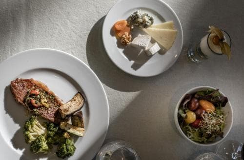 A serene dining table scene features gourmet dishes like steak with vegetables, cheese platter, and salad, ideal for a fine dining experience or culinary travel blog content.