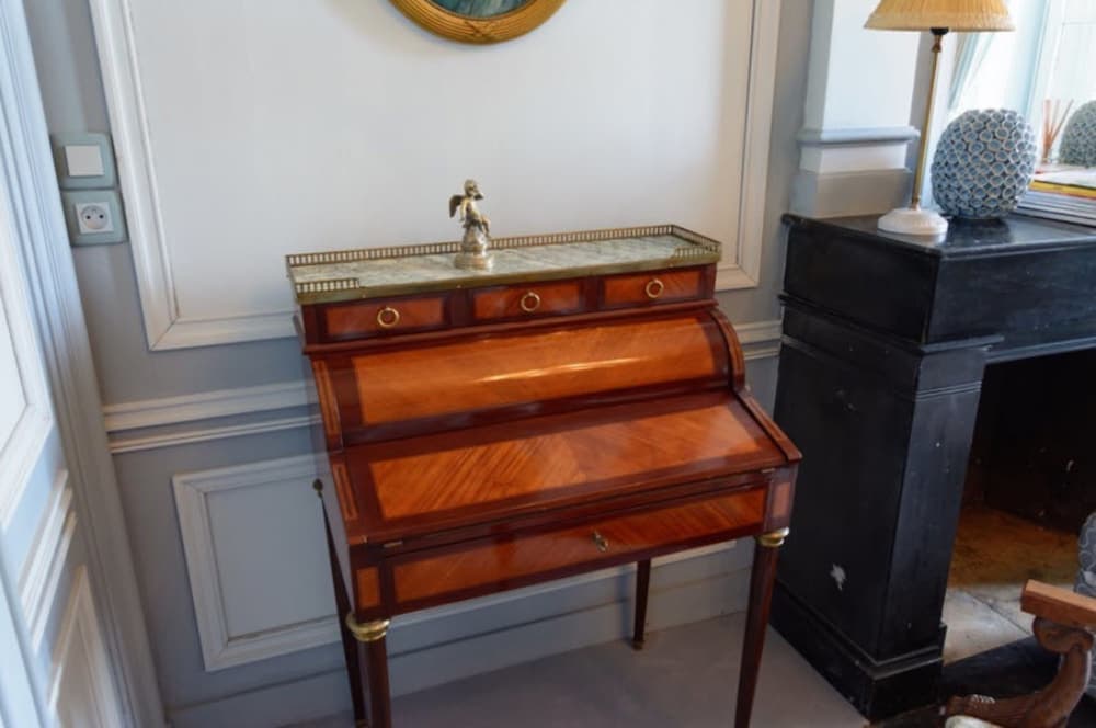 A cozy corner in an elegant room features a vintage wooden desk adorned with a small statue, set against light blue paneled walls, ideal for travelers seeking a charming writing space in a boutique hotel.