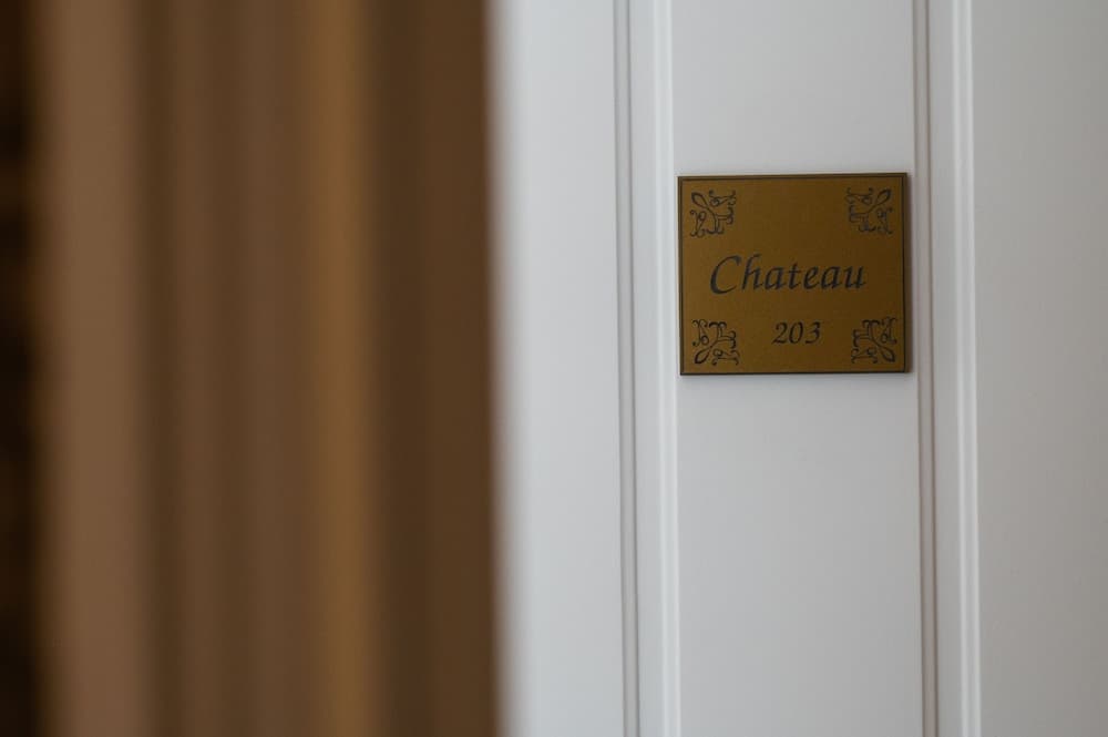 A close-up of an elegant brass plaque reading "Chateau 203" on a white door exudes sophistication, ideal for travelers seeking luxury accommodations in a boutique hotel setting.