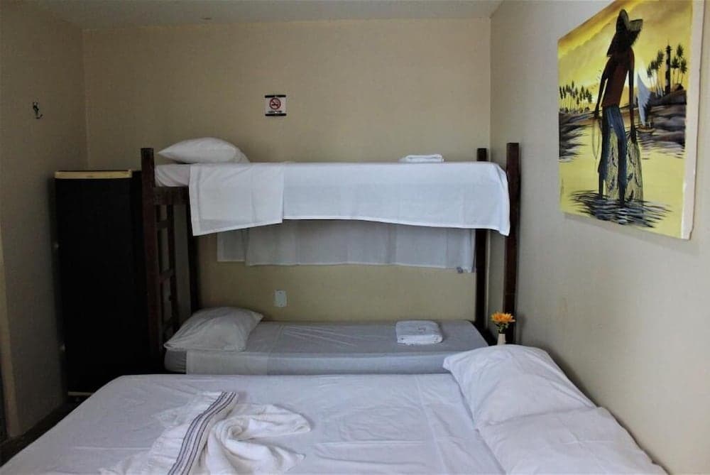 A cozy hostel room features bunk beds and a neatly made bed, adorned with tropical artwork, ideal for budget travelers seeking comfort in a compact space.