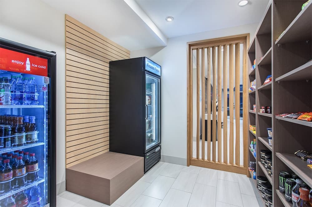 A modern convenience store aisle features a bright, organized layout with a wooden bench, beverage fridge, frozen food cooler, and shelves stocked with snacks, ideal for quick shopping trips.
