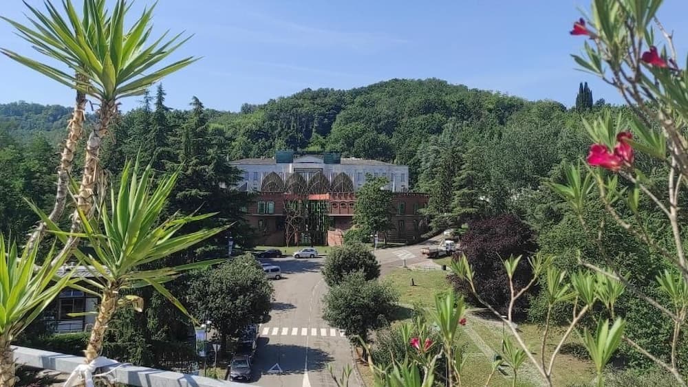 A serene resort nestled among lush green hills under a clear blue sky, framed by vibrant flowers and palm-like plants, offers an ideal getaway for relaxation and nature lovers.