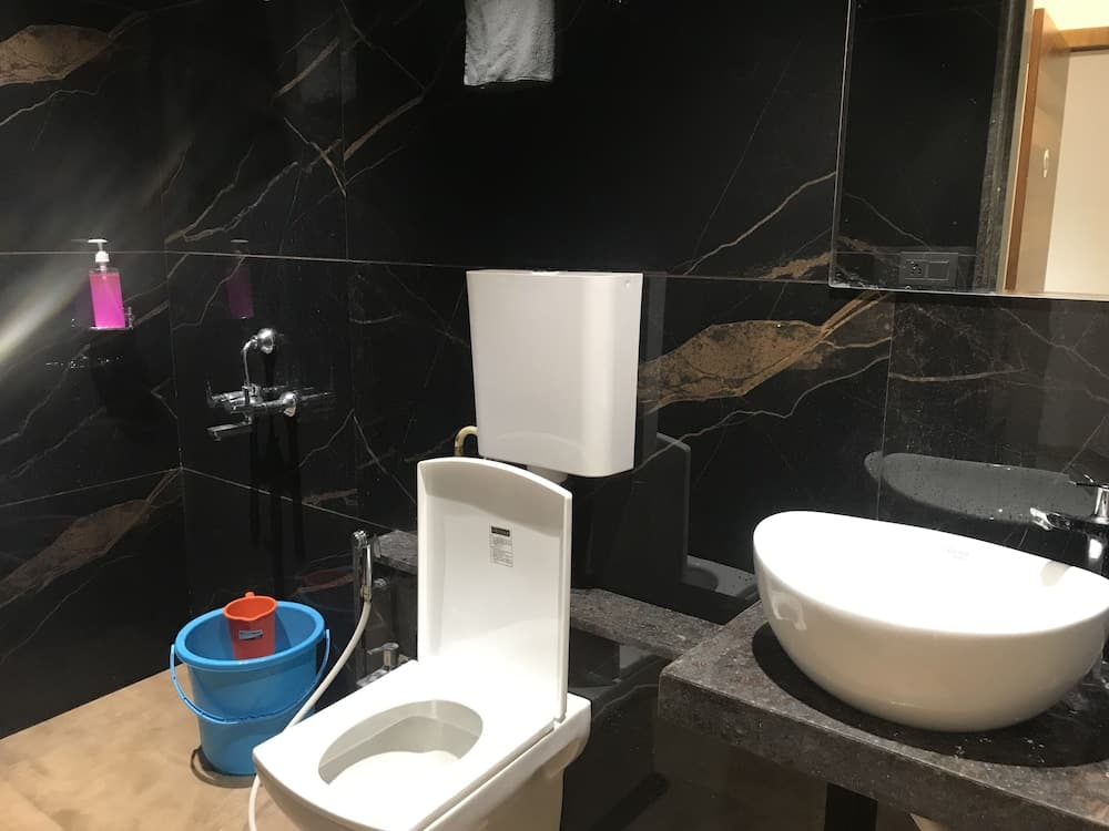 A modern bathroom with sleek black marble walls features a white toilet, sink, and a blue bucket with an orange cup, ideal for travelers seeking clean and stylish accommodations.
