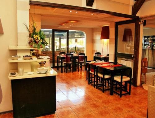 A cozy indoor restaurant with warm lighting, tiled floors, neatly arranged tables, and a welcoming buffet counter, ideal for travelers seeking a comfortable dining experience.