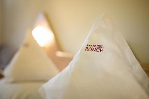 A cozy hotel room ambiance is captured with soft lighting and neatly arranged pillows featuring the "Hotel Ronce" logo, ideal for travelers seeking comfort and relaxation.