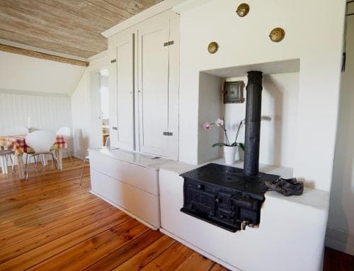 A cozy, rustic kitchen with wooden floors, white cabinetry, and a black wood-burning stove creates a warm and inviting atmosphere, perfect for travelers seeking a charming countryside retreat.