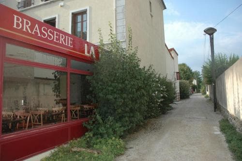 A quaint European brasserie with red accents invites travelers to dine along a serene, tree-lined alleyway, perfect for exploring local culinary delights in a peaceful setting.