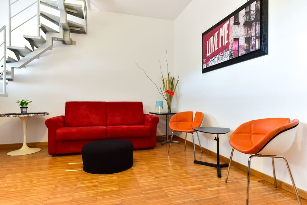 A cozy living room with vibrant red furniture, modern orange chairs, and a staircase in the background creates an inviting atmosphere ideal for travelers seeking stylish accommodation.