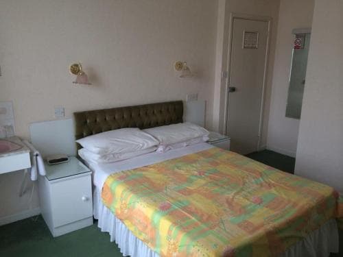 A cozy hotel room features a neatly made bed with a colorful quilt, a desk with a chair, and wall-mounted lamps, ideal for travelers seeking a simple and functional accommodation.