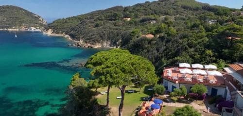 A serene coastal retreat features lush greenery, turquoise waters, and charming white buildings with red roofs, ideal for a relaxing beachside vacation.