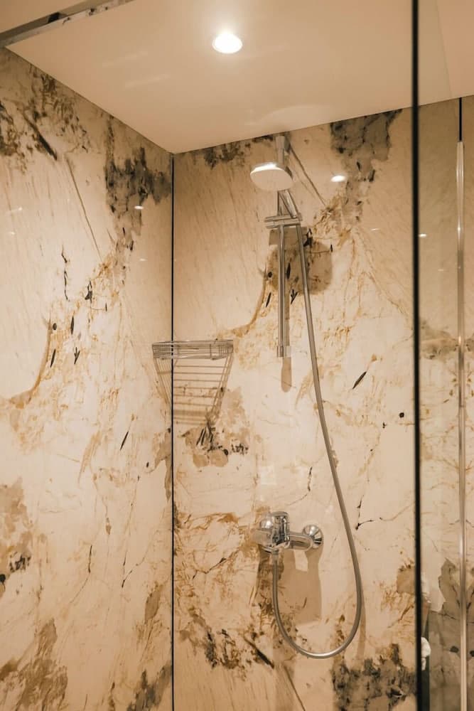 A luxurious bathroom features elegant marble walls, a sleek glass shower enclosure, and modern fixtures, creating an inviting and sophisticated space ideal for travelers seeking premium accommodations.