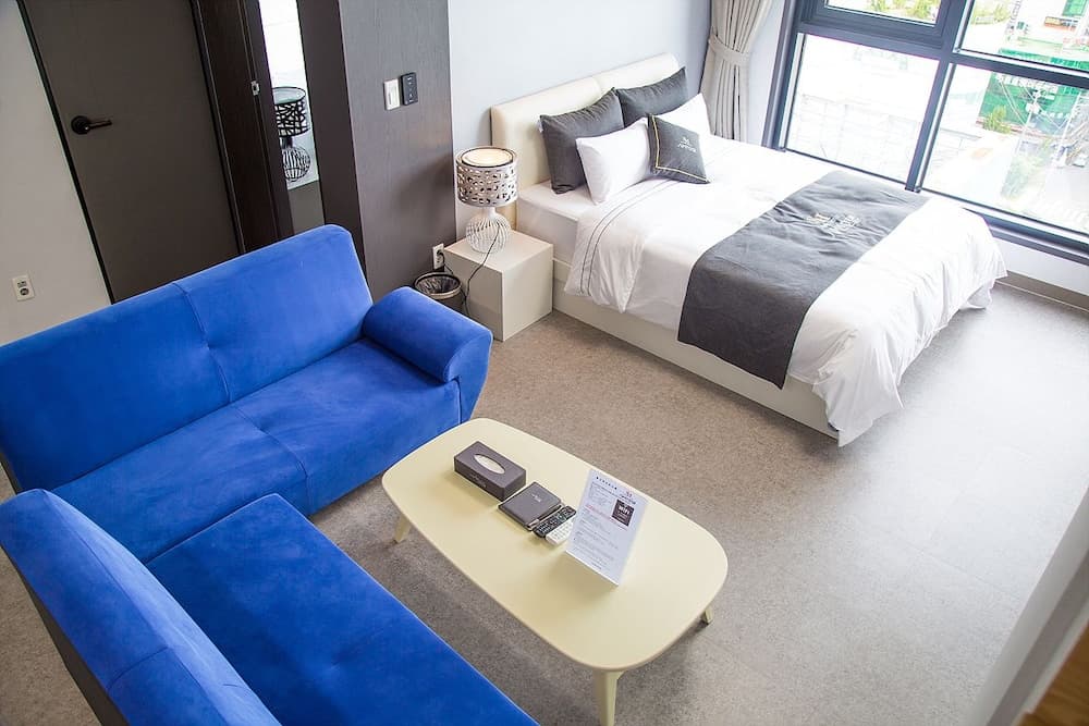 A cozy hotel room features a vibrant blue sofa, a neatly made bed with gray accents, and a modern coffee table, creating a welcoming atmosphere ideal for travelers seeking comfort and relaxation.