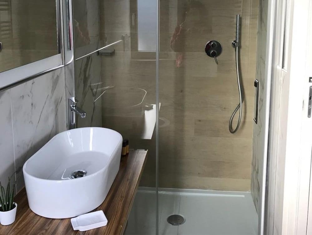 A modern bathroom features a sleek white sink on a wooden countertop beside a glass-enclosed shower with beige tiles, creating a clean and contemporary atmosphere ideal for travelers seeking comfort and style in their accommodations.