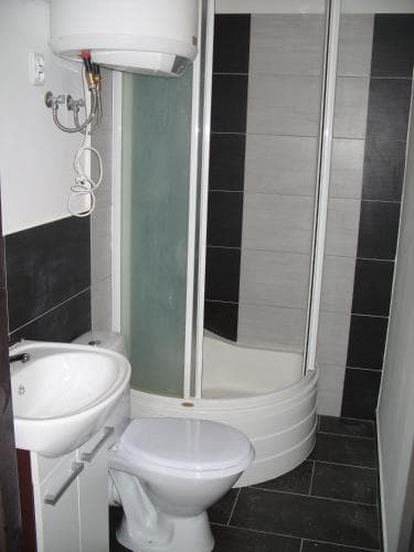 A compact bathroom with sleek black and white tiles, a corner shower enclosure, a sink, and a toilet, exudes a modern and functional vibe ideal for travelers seeking efficient accommodation amenities.