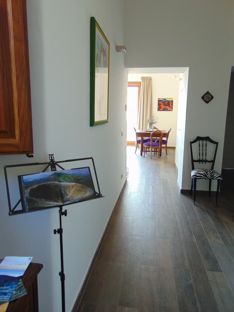 A cozy indoor hallway leads to a warmly lit dining area, featuring wooden floors, a music stand with scenic artwork, and inviting furniture, perfect for a relaxing vacation rental experience.