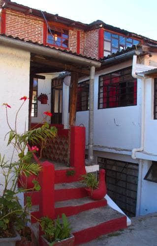 A cozy, vibrant guesthouse entrance with red-painted steps and potted plants invites travelers to explore its charming, rustic ambiance in a serene neighborhood setting.