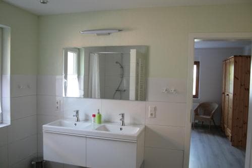A cozy bathroom with a double sink, mirror, and soft lighting creates a serene atmosphere, ideal for travelers seeking comfort in a private accommodation setting.